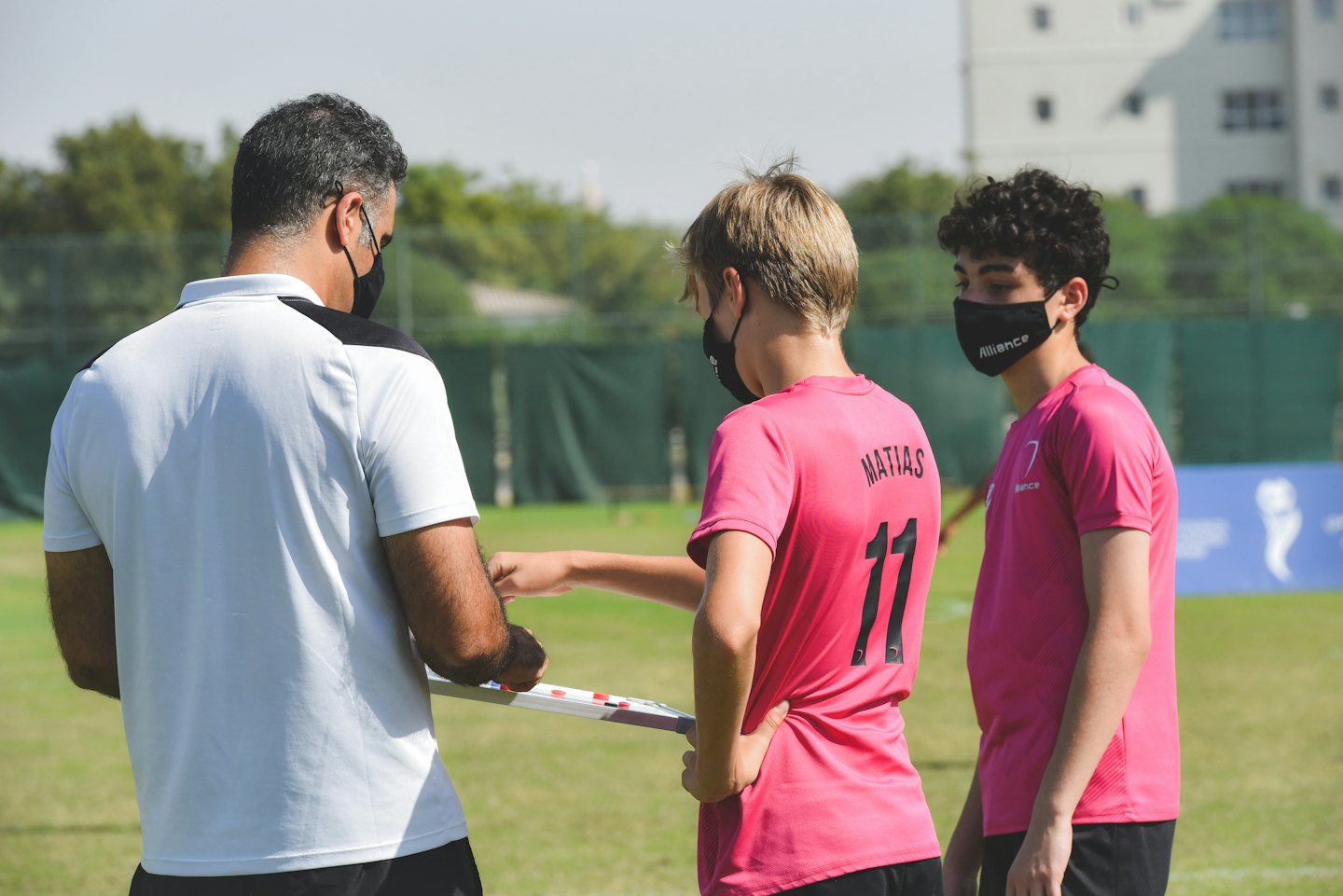 コーチが晴れたスポーツフィールドでホワイトボードを使って若い選手たちを指導している。